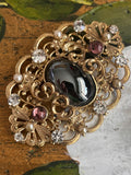 Vintage gold baroque-style brooch with black cabochon and rhinestones on gold-colored filigree